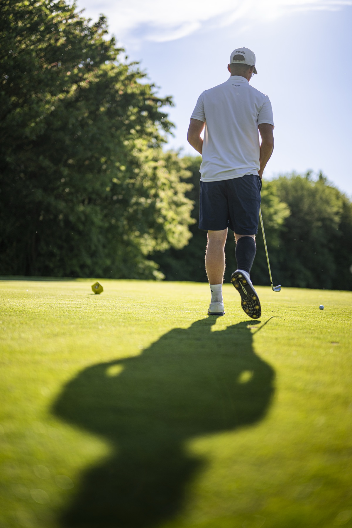 Spieler geht nach dem Abschlag über das Tee, langer Schatten auf dem Rasen
